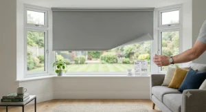 A close-up, photorealistic view of a white easy fit roller blind no-drill clip mechanism being adjusted by hand on a white uPVC window frame, with soft natural light.